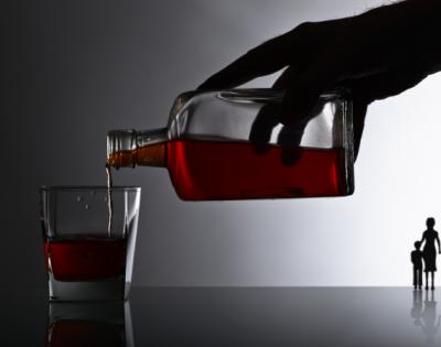 Hand pouring alcohol from a bottle into a glass with small outline of mother and child in the distance