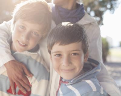 Two young sons stand in front of their mother who has her arm wrapped around them