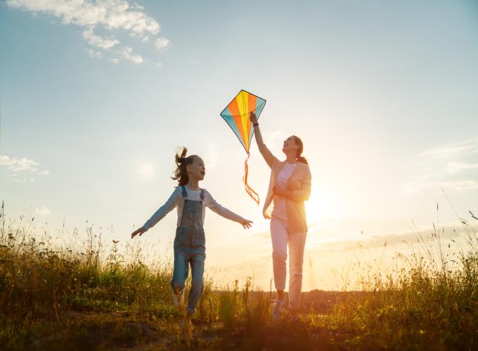 Women and girl flying a kite with the sunset behind them